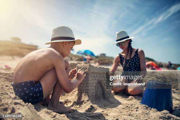 enfants ayant l’amusement construisant des châteaux de sable sur la plage - château de sable photos et images de collection