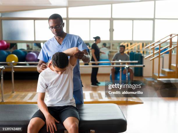 proveedor de atención médica estirando brazo de niño adolescente - black massage therapist fotografías e imágenes de stock