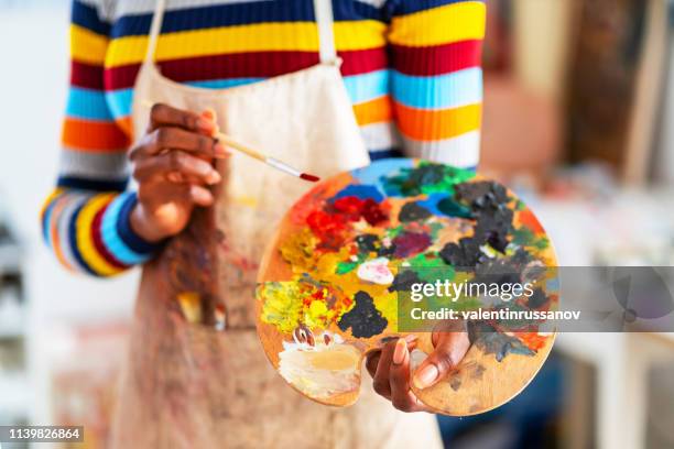 sorridente giovane donna afro che tiene tavolozza dei colori e pennello - dipinto in acrilico foto e immagini stock