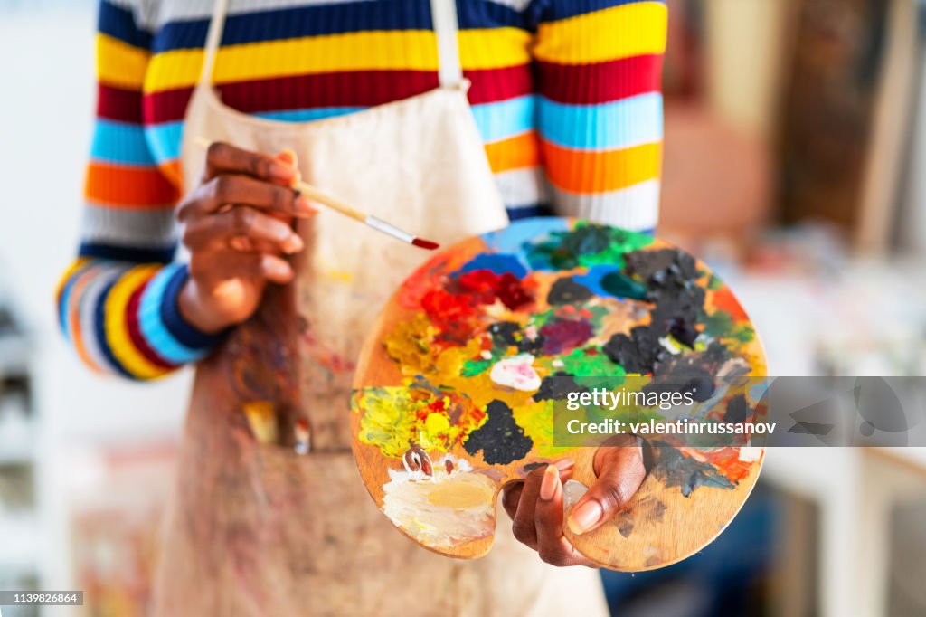Smiling young afro woman holding color palette and paintbrush
