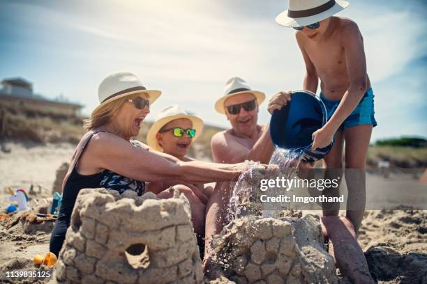 grands-parents et petits-fils jouant ensemble dans le sable sur la plage - château de sable photos et images de collection