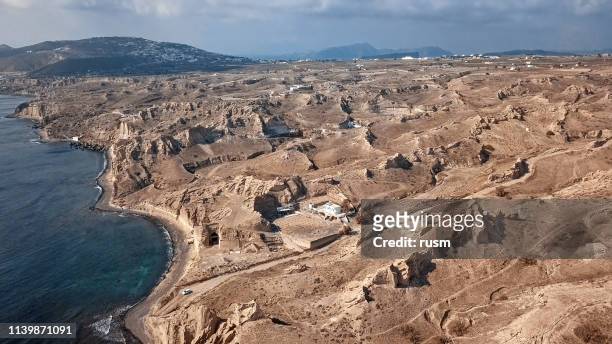 panorama aéreo de tierras áridas y acantilados de arena en la playa de vlihada en la isla de santorini, grecia - akrotiri fotografías e imágenes de stock