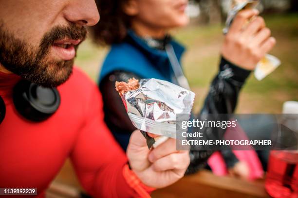 active young couple eating a protein snack bar together - candy wrapper stock pictures, royalty-free photos & images