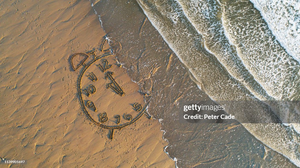 Clock drawn in sand at water's edge