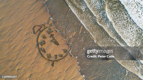 clock drawn in sand at water's edge - daylight saving time foto e immagini stock