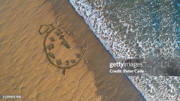 clock drawn in sand at water's edge - holiday hours stock-fotos und bilder