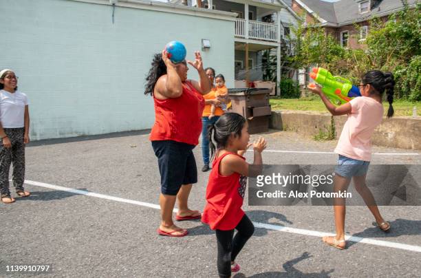 the big happy latino, mexican-american family - the mother, body-positive optimistic smiley woman, her sister, and kids, girls of different ages - playing outdoor with a water gun and having fun - hot mexican girls stock pictures, royalty-free photos & images