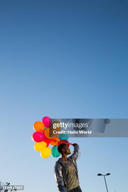 vertical view of young woman holding colorful balloons on blue sky background - african american women in the wind stock pictures, royalty-free photos & images