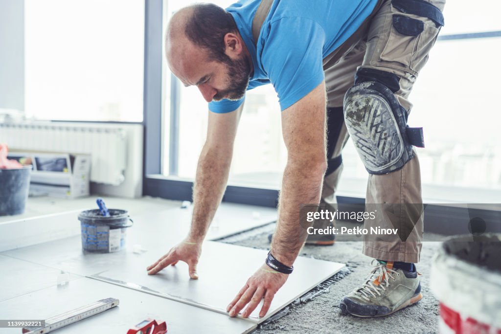 Ouvrier de tuile posant des tuiles sur le plancher