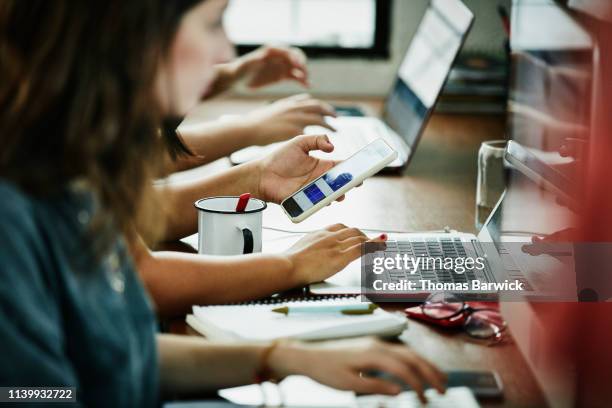 businesswoman checking app on smart phone while working on web design in studio - studio di design foto e immagini stock