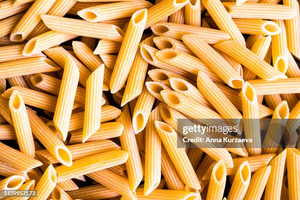 heap of uncooked whole wheat penne italian pasta, top view. pasta pattern. food background. - rigatoni stock-fotos und bilder