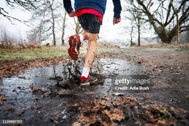 rear view of teenage boy running through puddle splashing - poça imagens e fotografias de stock