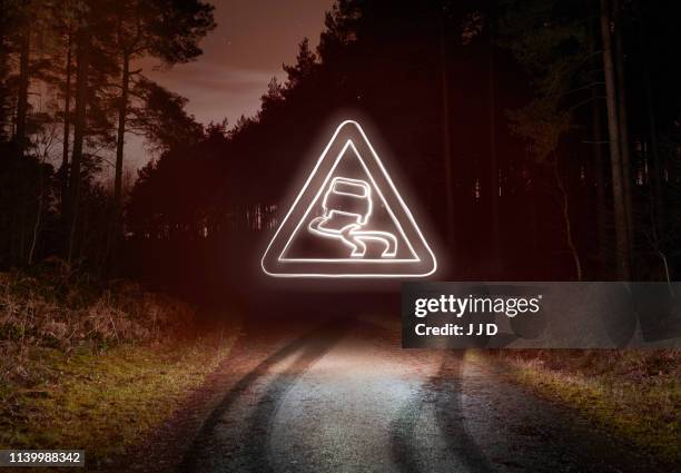 tyre skid marks and glowing slippery warning sign above forest road at night - warning sign stock pictures, royalty-free photos & images
