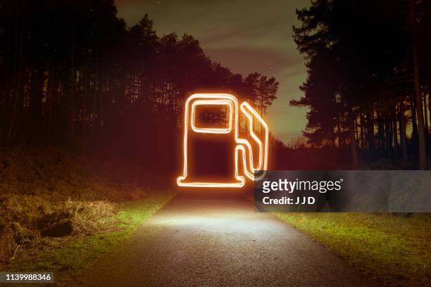 glowing gas pump symbol above forest road at night - night before fotografías e imágenes de stock