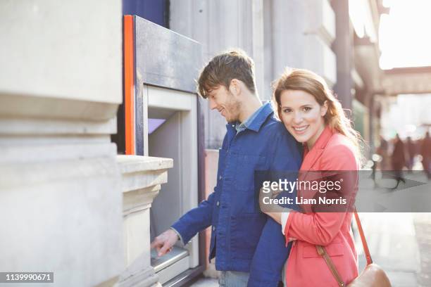 couple withdrawing money from street cash machine, london, uk - man atm smile stock pictures, royalty-free photos & images