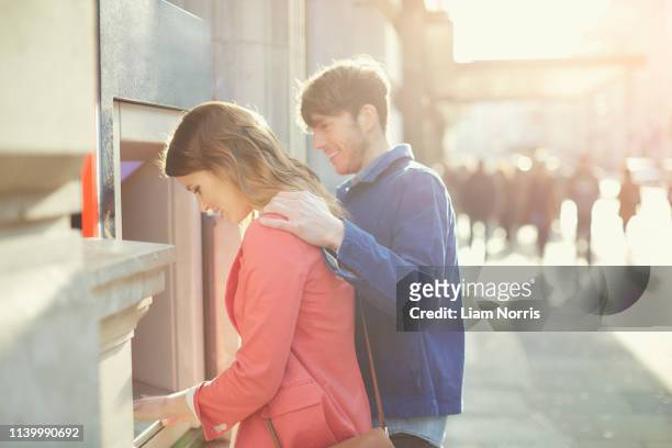 couple withdrawing money from cash machine on street, london, uk - man atm smile stock pictures, royalty-free photos & images