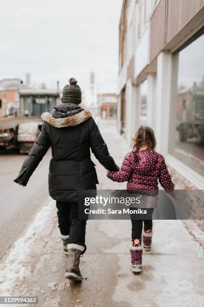 mother and daughter walking past shop in winter - holding hands in the snow stock pictures, royalty-free photos & images