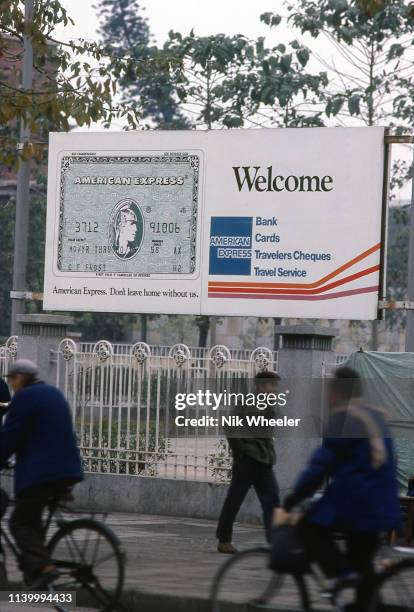Pedestrians walk past large billboard advertisement for American Express Credit Cards on street in Guangzhou, formerly Canton, circa 1980: