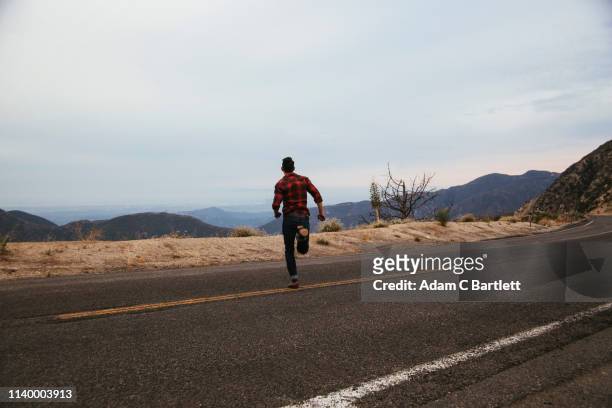 young man running across mountain road, los angeles, california, usa - fuggire foto e immagini stock