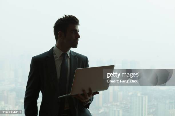 young businessman with laptop in front of skyscraper office window, shanghai, china - young man asian silhouette stock pictures, royalty-free photos & images