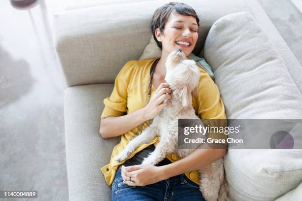 young woman hugging dog on living room sofa - yellow blouse stockfoto's en -beelden