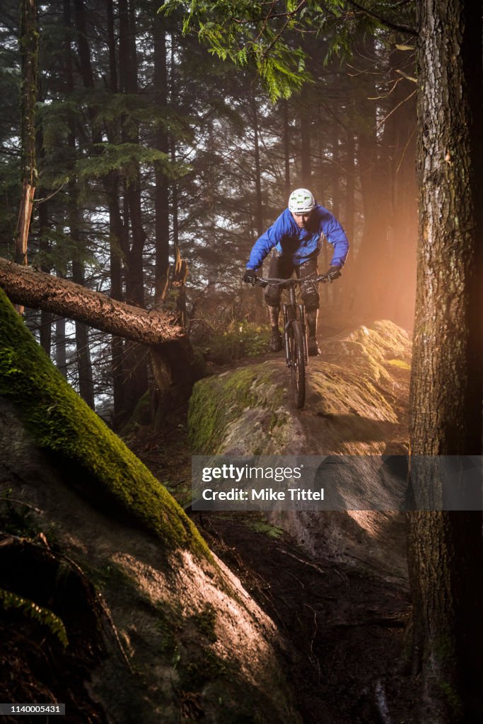 Young male mountain biker riding over forest boulders
