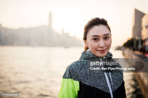 portrait of young woman wearing tracksuit top in front of water smiling - tracksuit jacket stock-fotos und bilder