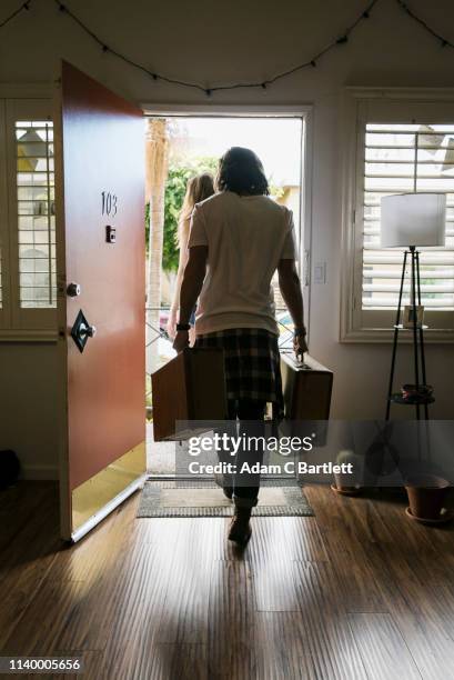 rear view of young couple carrying suitcases out of front door - carry on luggage photos et images de collection