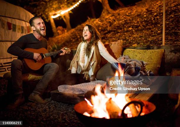 young couple next to fire and yurt singing and playing guitar - yurt stock pictures, royalty-free photos & images