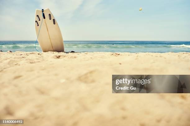 surface level view of surfboard upright in sand on beach - california beach stock-fotos und bilder