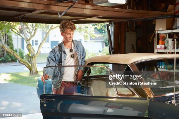 young man in garage opening door of vintage car - old car garage stock pictures, royalty-free photos & images