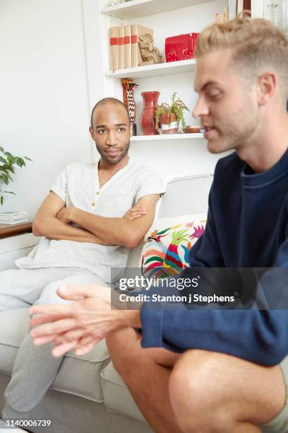 homosexual couple sitting on sofa having disagreement - lunch argument stock-fotos und bilder