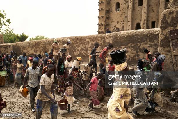 People take part in the annual rendering of the Great Mosque of Djenne in central Mali on April 28, 2019. - Several thousand residents of the...