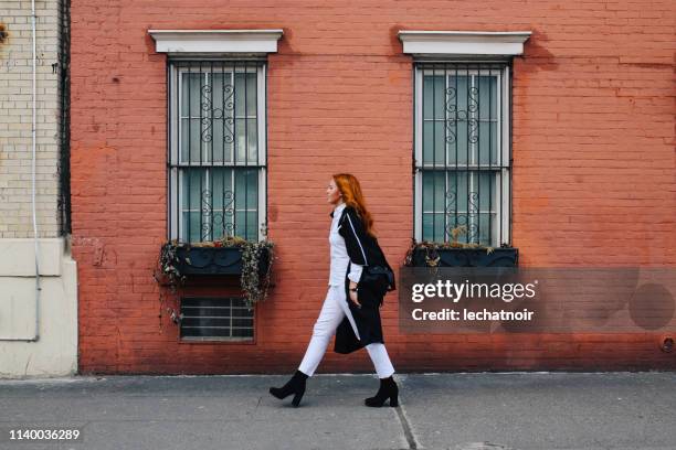 fashionable redhead woman walking by the brick wall building in west village, manhattan, ny - west front stock pictures, royalty-free photos & images