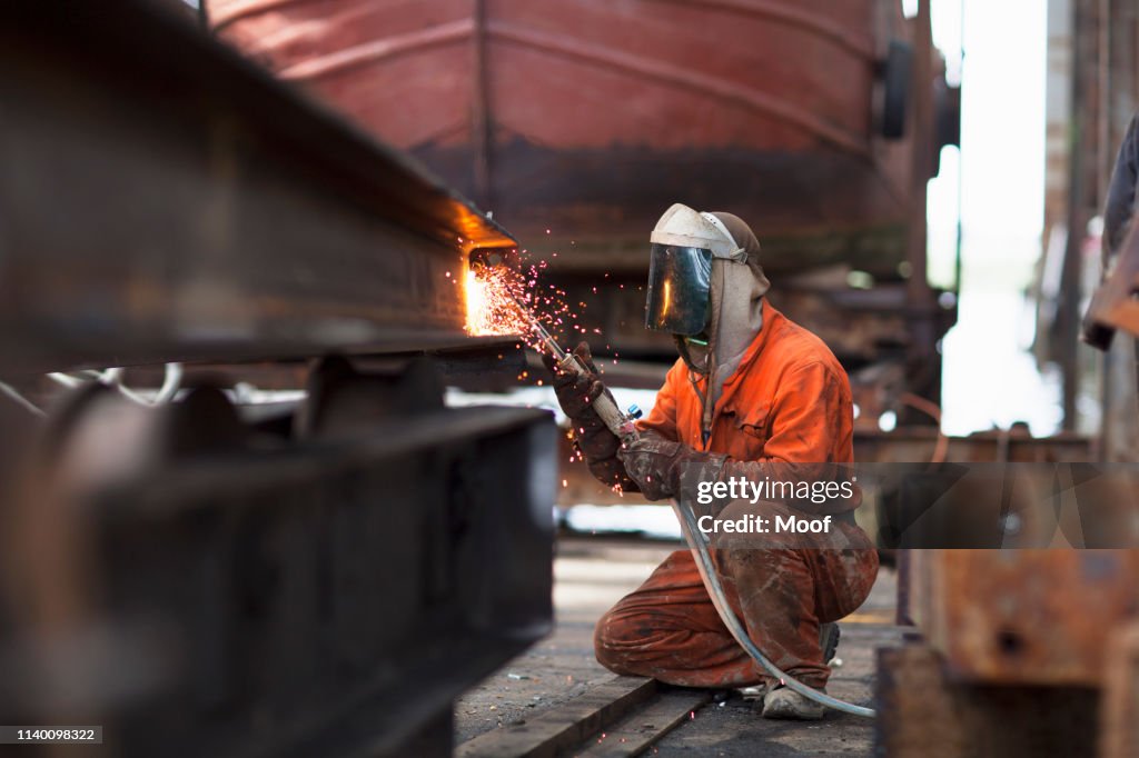 Welder welding girder in shipyard workshop