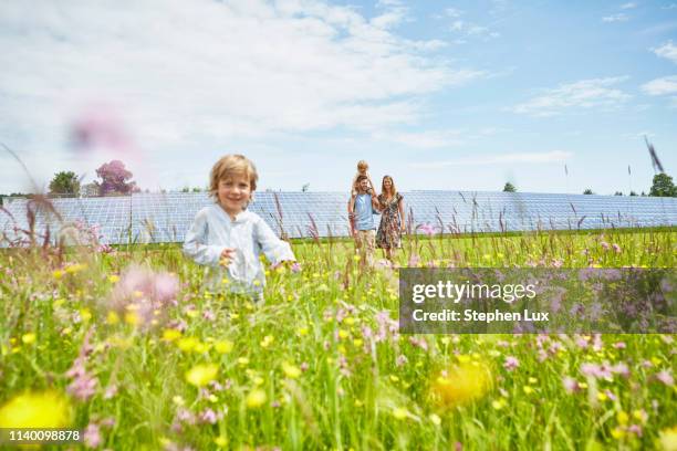 young boy running through field, mother, father and brother following behind, next to solar farm - ideas generation stock-fotos und bilder