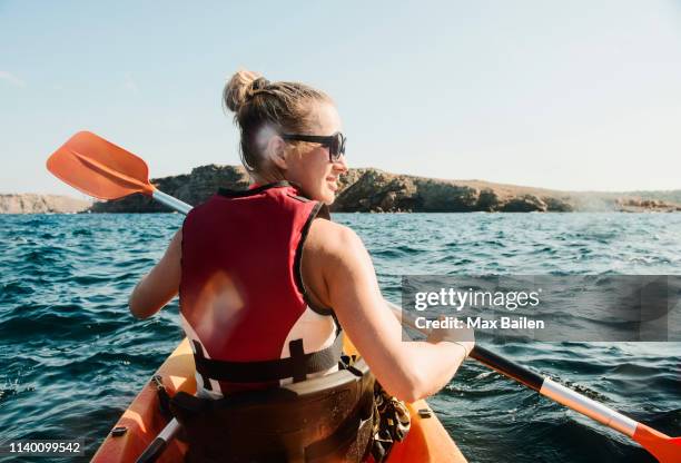 rear view of mid adult woman sea kayaking, menorca, balearic islands, spain - sea kayaking stock-fotos und bilder