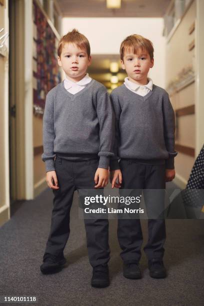 portrait of elementary schoolboy twins in school corridor - identical twin stock pictures, royalty-free photos & images
