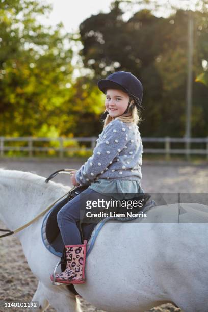 portrait of happy girl riding white pony in equestrian arena - riding hat stock pictures, royalty-free photos & images