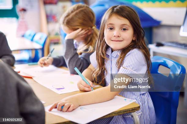 portrait of girl drawing at desk in elementary school - schooluniform stockfoto's en -beelden