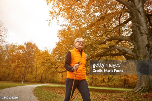 senior female nordic walker striding in autumn park - mobility walker stock-fotos und bilder