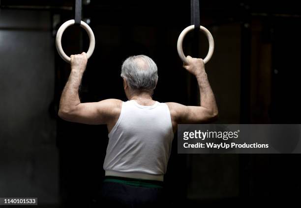 rear view of senior man holding gym rings in dark gym - tank top back stock pictures, royalty-free photos & images