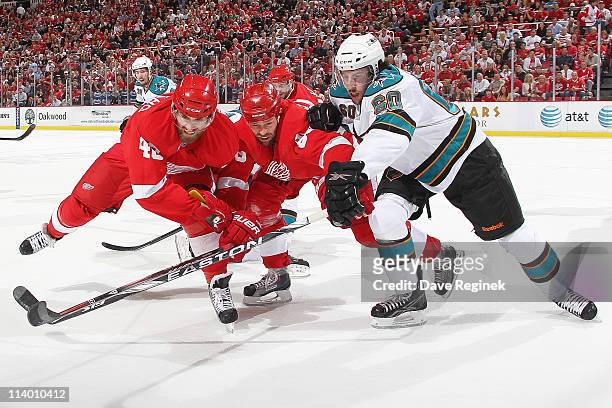 Henrik Zetterberg of the Detroit Red Wings and teammate Tomas Holmstrom reach after puck alongside Jason Demers of the San Jose Sharks during Game...