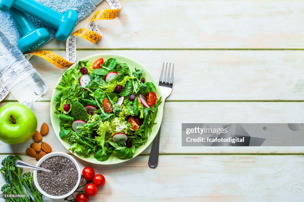 Healthy eating and exercising backgrounds: Fresh healthy salad, dumbbells and tape measure with copy space