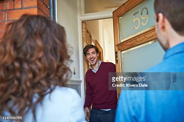 man welcoming friends at front door - visit stock pictures, royalty-free photos & images