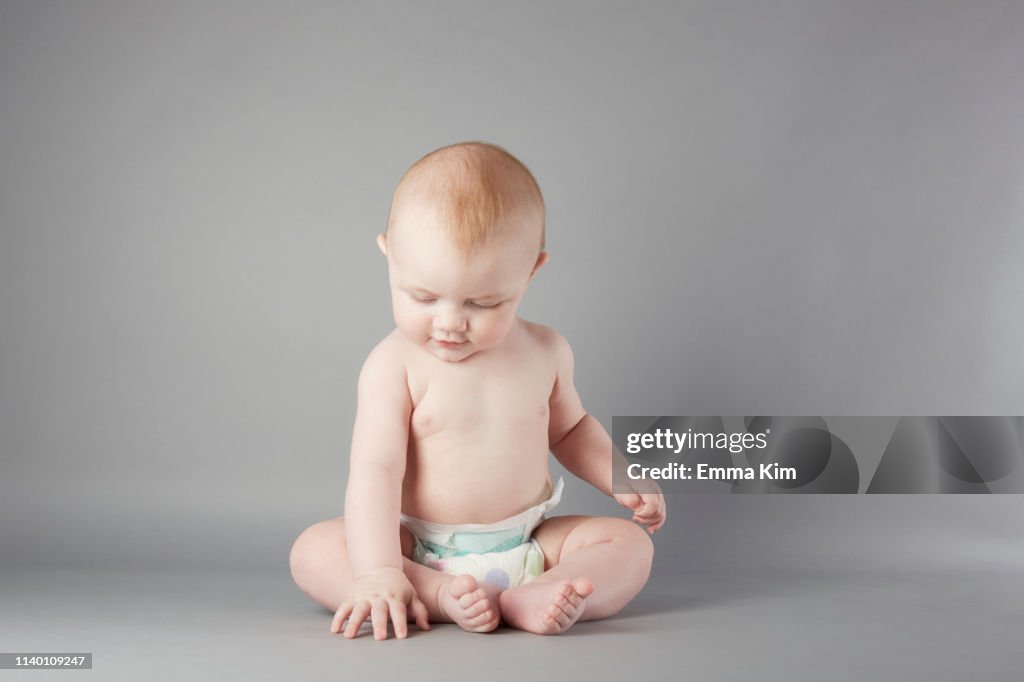 Studio portrait of baby boy sitting up and touching floor