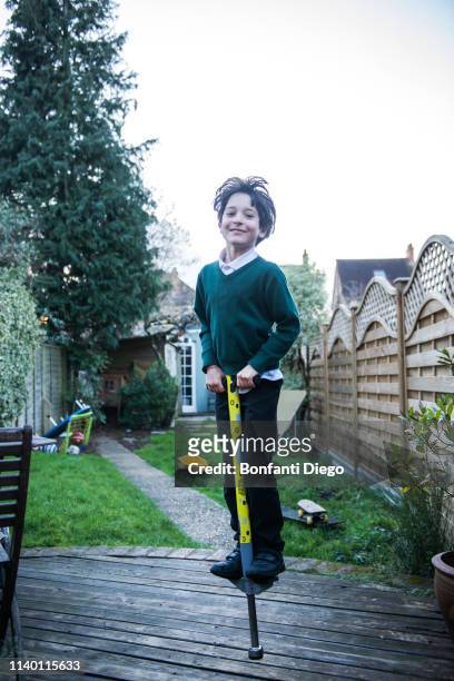 boy jumping on pogo stick in garden - pogo stock-fotos und bilder