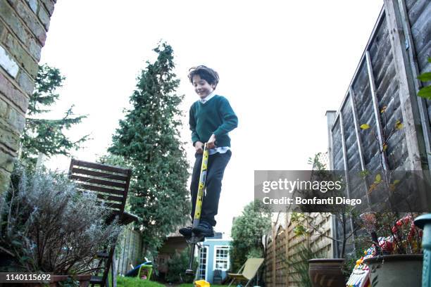 boy jumping on pogo stick in garden - pogo stock-fotos und bilder