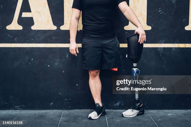 man with prosthetic leg leaning on wall in gym - amputé photos et images de collection