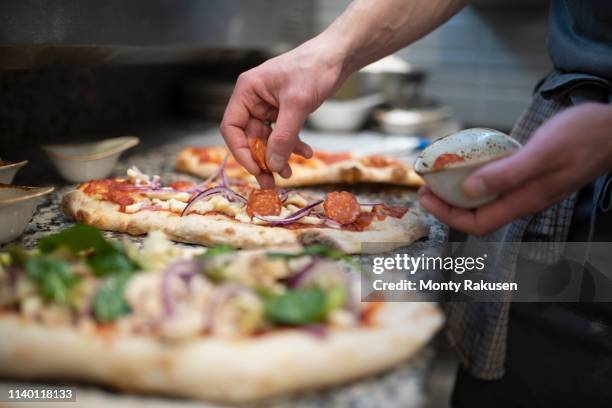 chef placing sausage onto pinsa romana base, a roman style pizza blend reducing sugar and saturated fat, containing rice and soy with less gluten, close up of hands - italiaanse keuken stockfoto's en -beelden